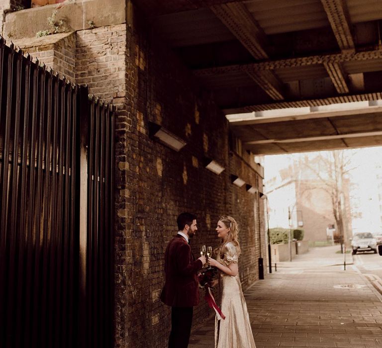 Bride and groom stand drinking outside their city wedding venue