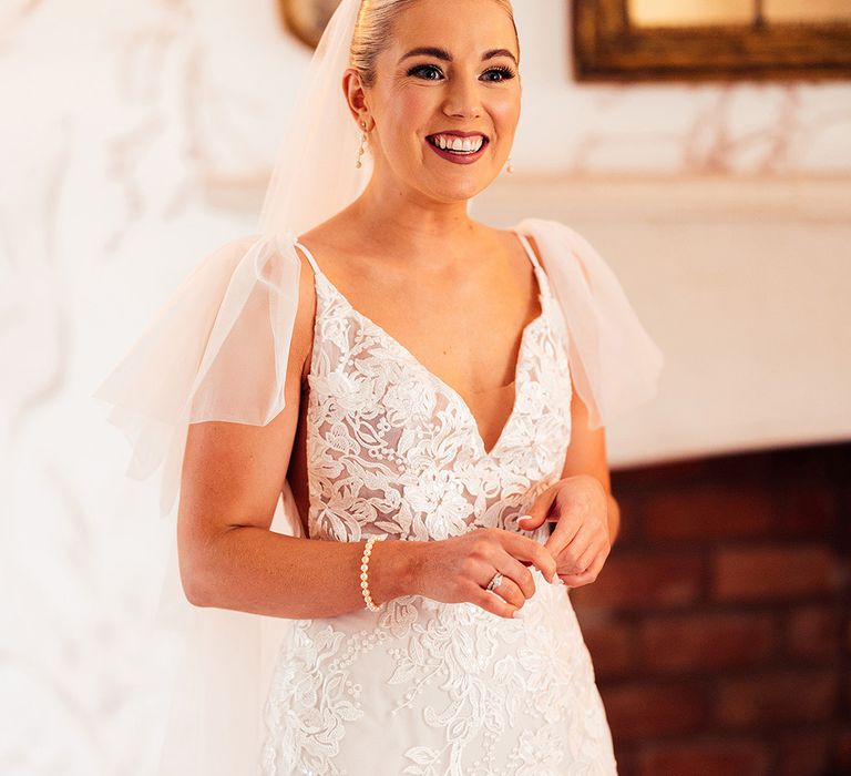 Bride with sleek blonde updo, smoky eyes and darker lip with lace wedding dress from Emmy Mae with pearl bracelet