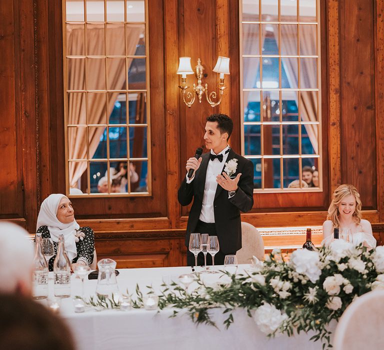 Groom in black tie stands reading out his speech