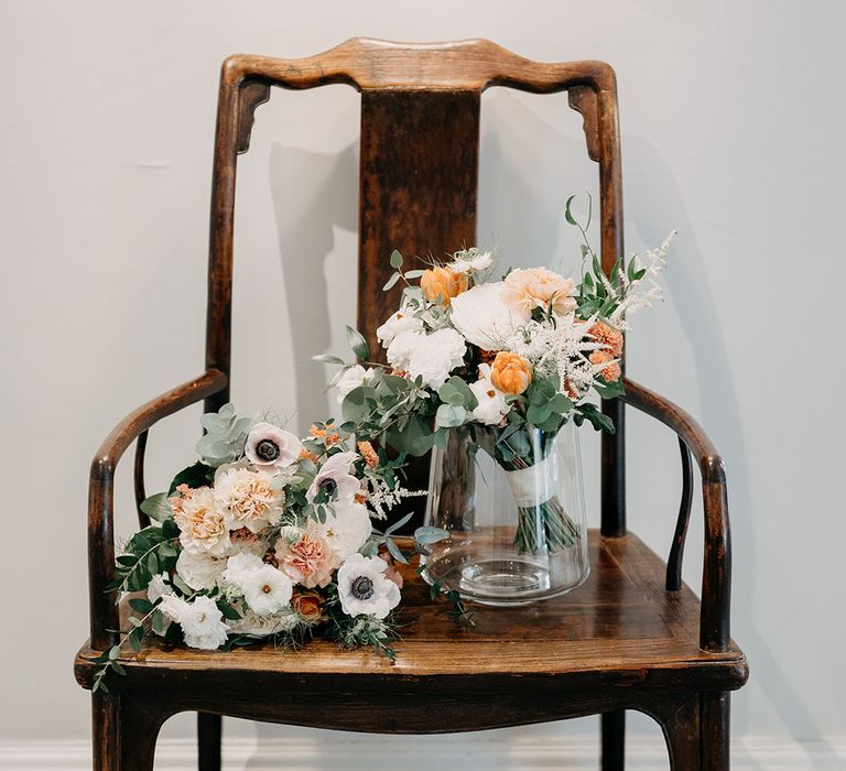 Wooden chair with bridal bouquets atop with white and orange blooms 