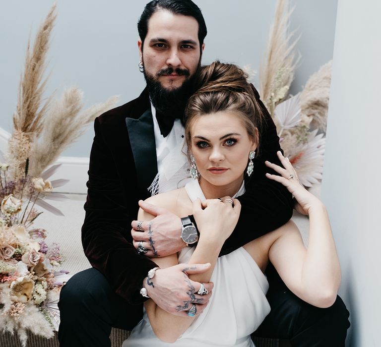 Groom in a tuxedo embracing his bride in a satin halterneck wedding dress