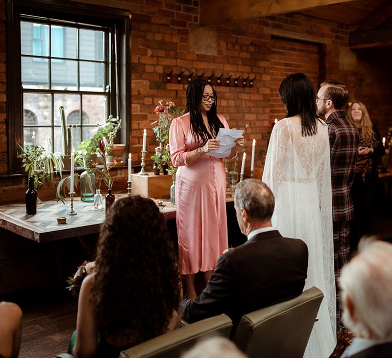 Bride & groom during civil ceremony at The Chimney House as bride wears lace cape and groom wears bespoke tartan suit 