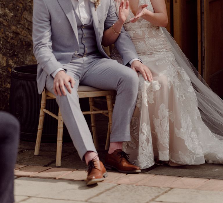 Groom wears light grey three piece suit complete with dried floral buttonhole sits besides his groom wearing Jane Hill wedding dress 