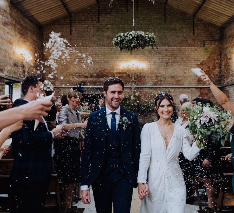 Bride and groom exit from their wedding ceremony to white confetti 