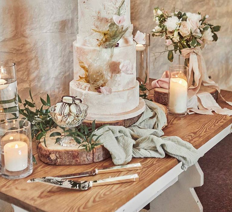 Dessert table with 3-tired wedding cake with exquisite sugar paste, spun sugar and rice paper work on a rustic tree slice 