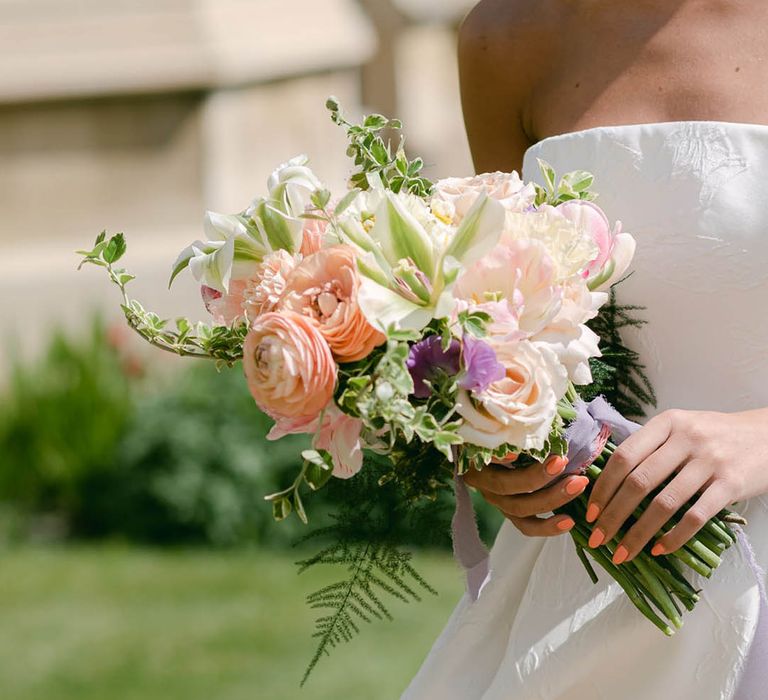 Bride with coral pink wedding nails holds a pastel wedding bouquet with roses and lilies 