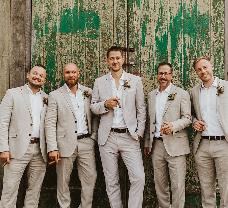 Groom standing with the groomsmen in matching light suits holding cigars 