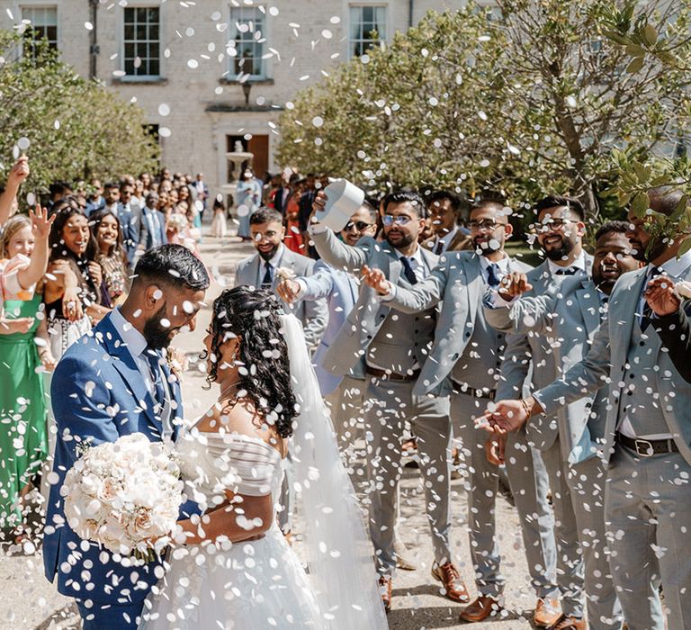 Bride & groom embrace as white confetti is thrown around them by wedding guests 