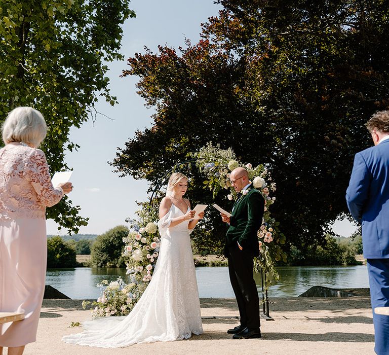 Bride & groom during outdoor wedding ceremony in front of floral archway 