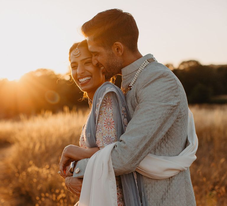 Groom embraces his bride in golden fields during couples portraits as the sun begins to set