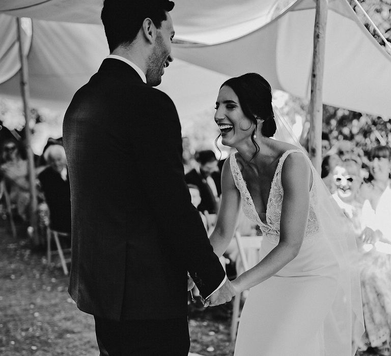 The bride laughs during the ceremony while she holds hands with the groom 