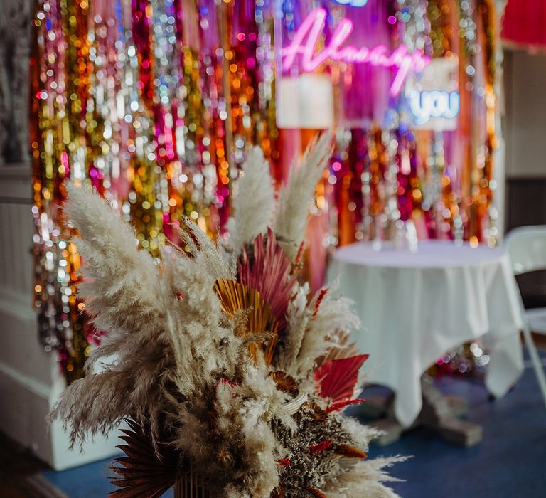 White pampas grass and autumnal bouquet and metallic metallic streamer backdrop with pink neon sign in the background