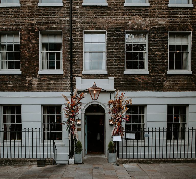 The Zetter Townhouse with large floral arch with roses, peonies, foliage and pampas grass in orange, red, yellow and green