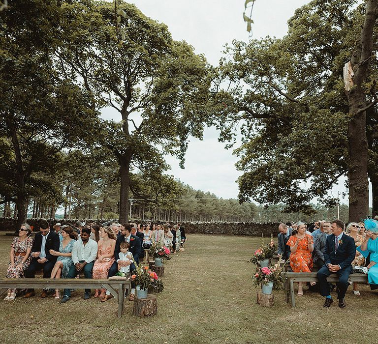 Wedding guests sit on wooden benches for the outdoor wedding ceremony at a farm 