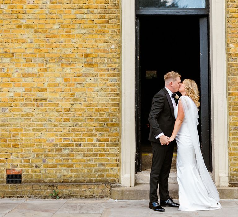 Bride & groom embrace outdoors as bride wears pearl embellished wedding cape 