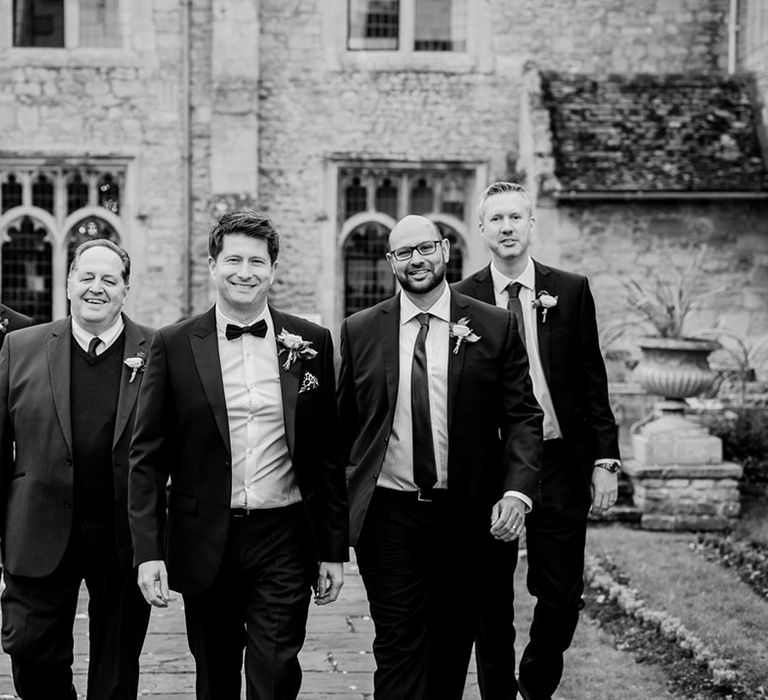 Groom in black tie walking with the groomsmen in mismatching suits for the winter Christmas wedding 