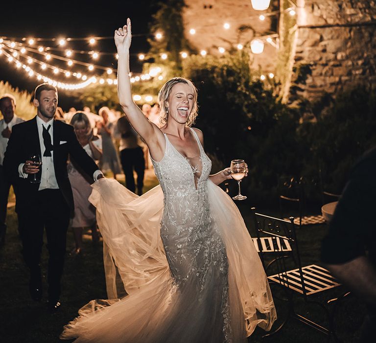 Bride in plunge neck lace wedding dress dances alongside her groom in black-tie