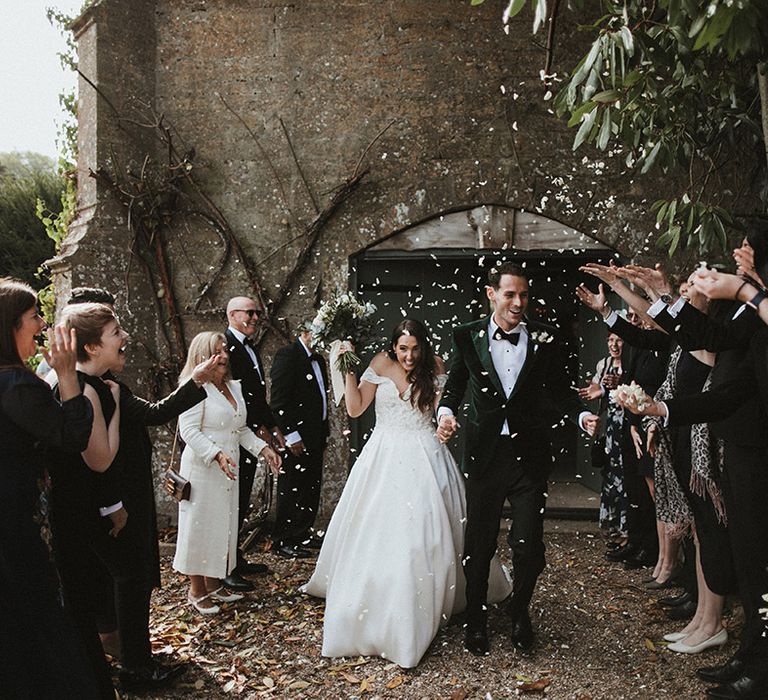 Classic and traditional wedding with the groom in a dark green tuxedo and bow tie align with the bride in luxe off the shoulder wedding dress to confetti 