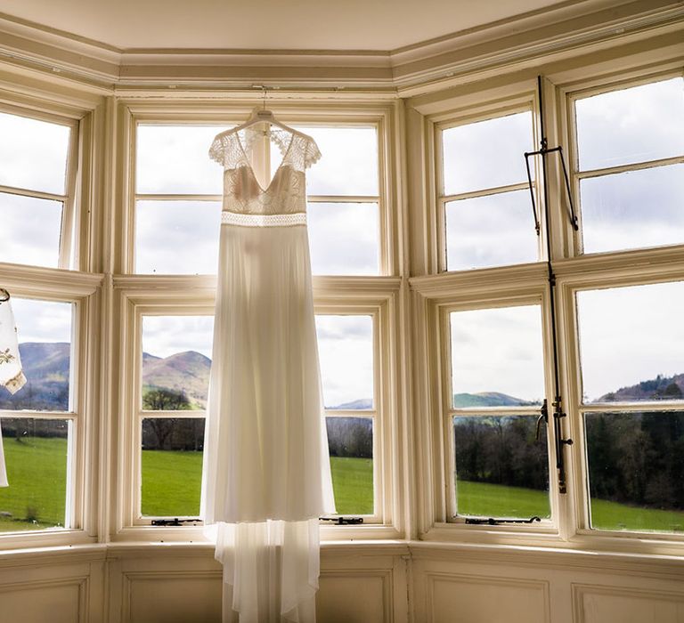 Lace wedding dress with capped sleeves hangs beside flower girl dress made from Mother Of The Bride's wedding dress