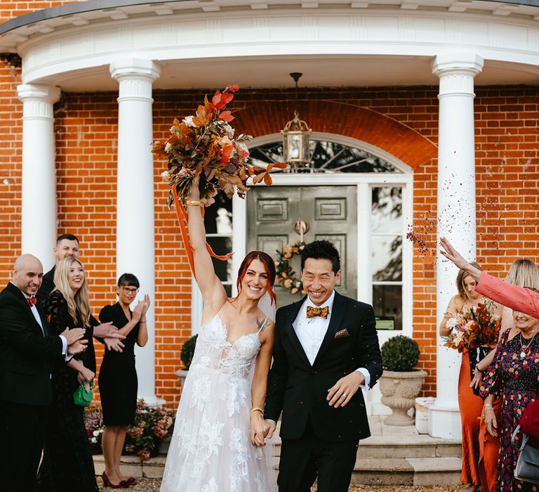 Bride in sheer floral styled wedding dress walks alongside her groom in black tie after wedding ceremony  