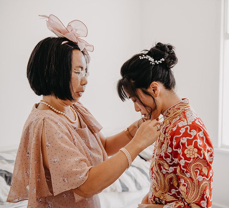 Mother of The Bride helps her daughter get ready in traditional red Chinese wedding dress