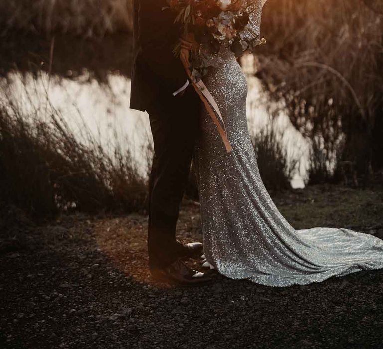 Bride in sparkly wedding dress and groom in classic black tuxedo doing couples golden hour photoshoot 