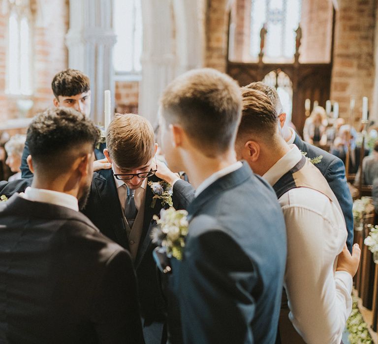 The groomsmen all pray around the groom before the wedding ceremony in matching navy suit jackets 