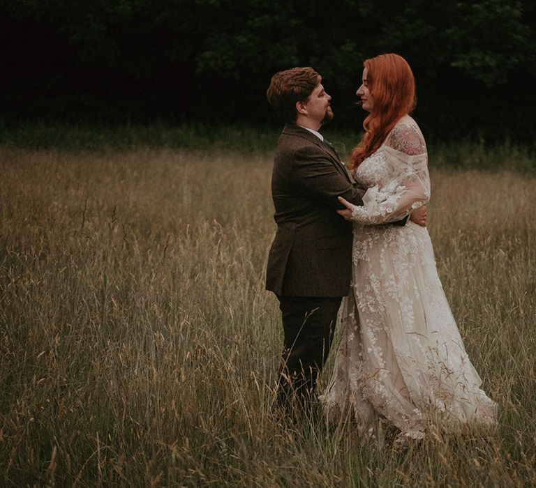 Groom in three piece suit embracing the bride in a boho off the shoulder long sleeve wedding dress with floral lace 