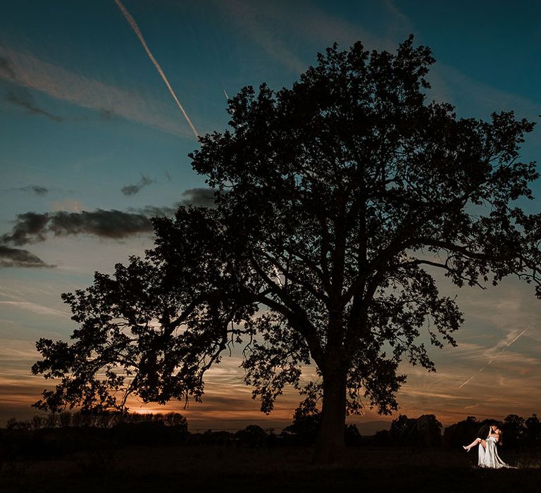 Groom sweeps the bride in for a kiss against the stunning backdrop of Lincolnshire at dusk 