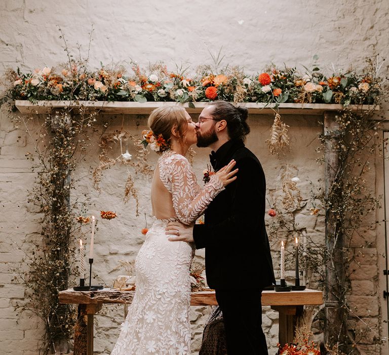 Wedding altar decorated with Persian rugs, autumnal wedding flowers and black candles with the bride and groom sharing their first kiss as a married couple