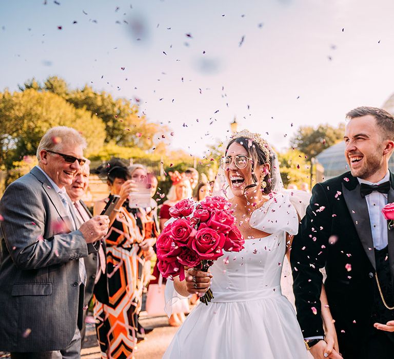 Bride in ruffle Emma Beaumont wedding dress with pink rose bouquet walking back down the aisle with the groom in a black tuxedo 