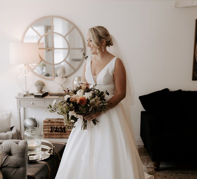 Bride in a Maggie Sottero wedding dress with pearl necklace, earrings, and other jewellery holding a neutral bridal bouquet 