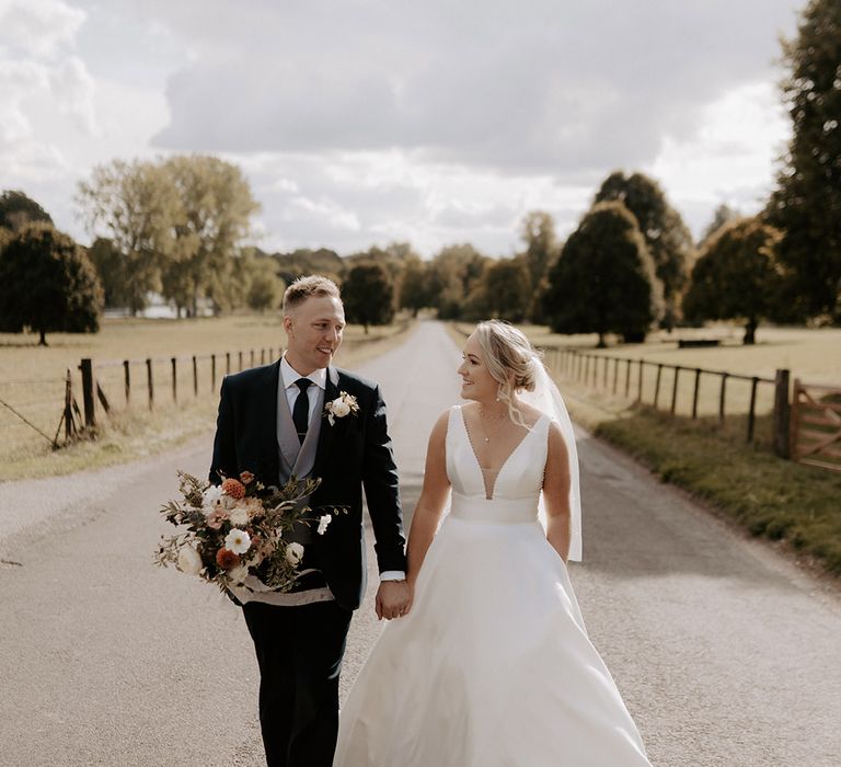 Bride in plunging Maggie Sottero wedding dress with the groom in a three piece black and grey suit holding the bridal bouquet 