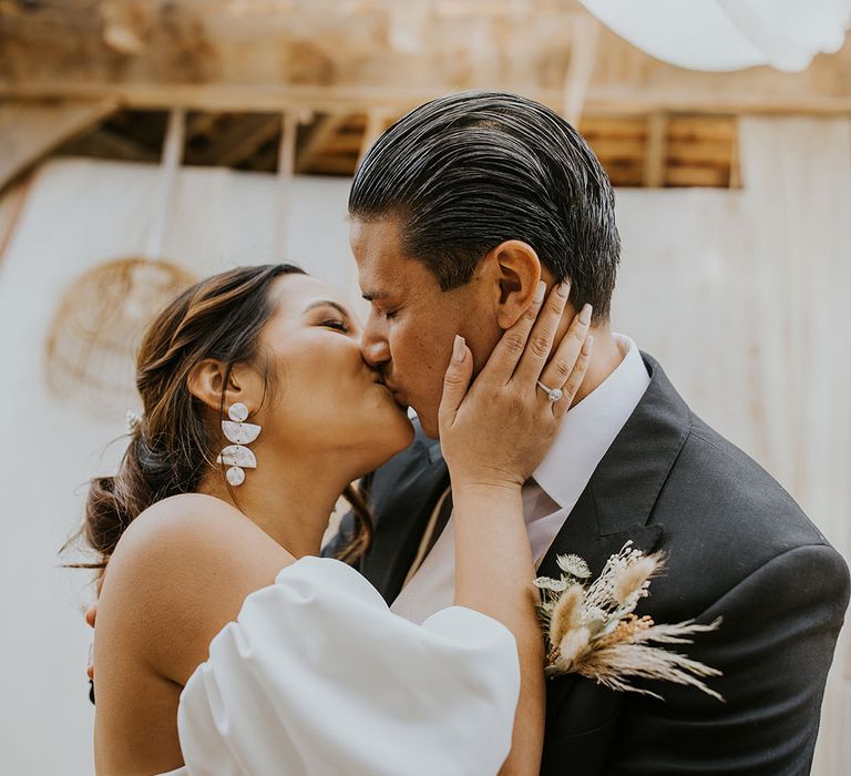 bride in a puff sleeve wedding dress kissing her groom 