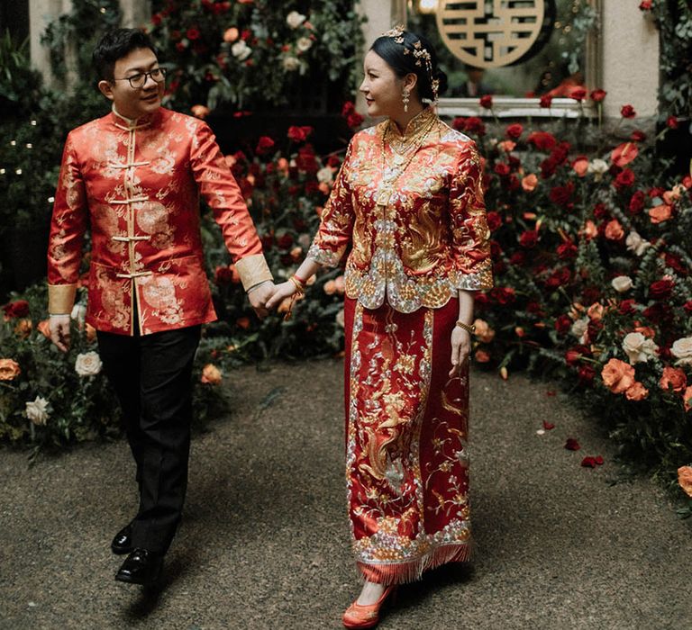 Bride in red and gold stunning wedding outfit walling hand in hand with the groom in matching outfit at Vancouver wedding in Canada 