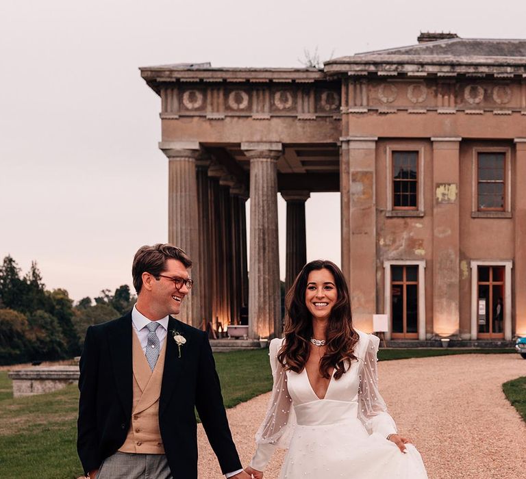 The bride and groom walk hand in hand around their mansion wedding venue in Hampshire 