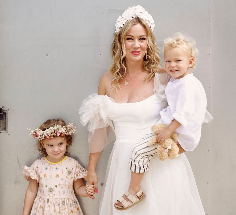 Bride in Halfpenny London wedding dress with white flower bridal crown and earrings holding her two children on her wedding day 