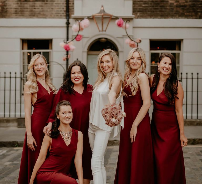 Bride in white bridal trousers and top with dark red bridesmaid autumnal dresses