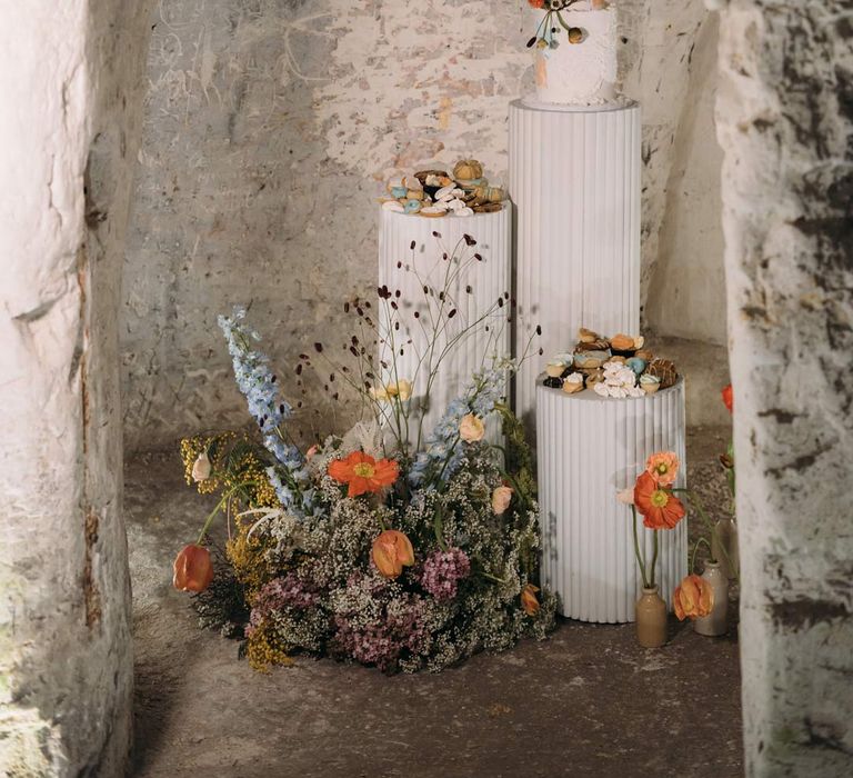 An assortment of wedding cakes and wedding desserts on white ribbed cake stands and large dried flower arrangement at Margate Caves 