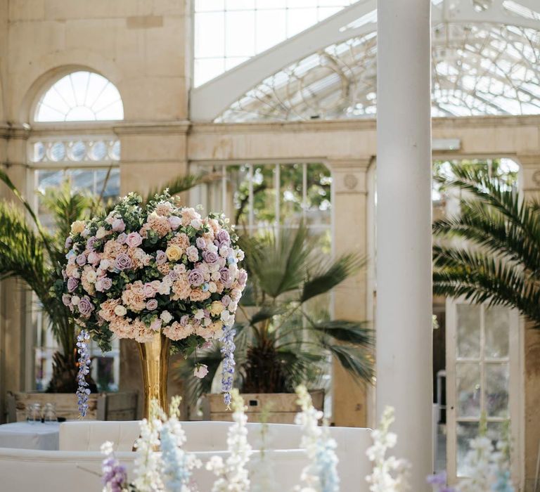 Syon Park wedding venue reception room with suspended pastel florals and tropical plants 