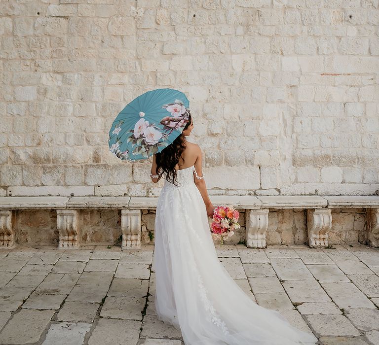 Bride in 3D lace wedding dress holds turquoise South Asian umbrella and wedding bouquet full of blush and pink peonies