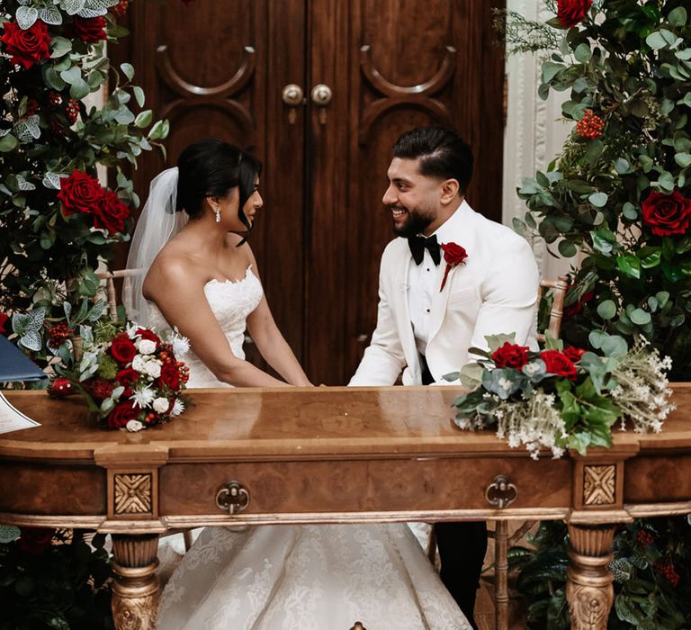 The bride and groom look into each other's eyes as they sit at the table to sign the register 