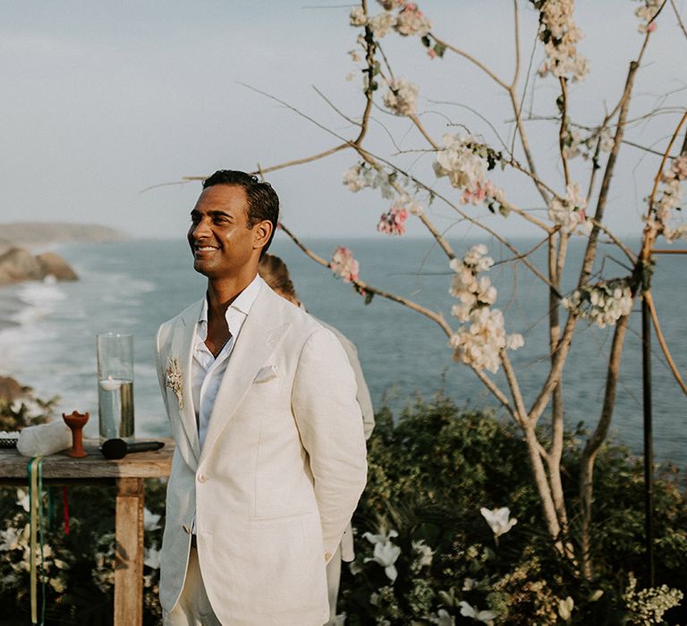 Groom in cream wedding suit waits at altar for bride during Tigre Del Mar wedding ceremony