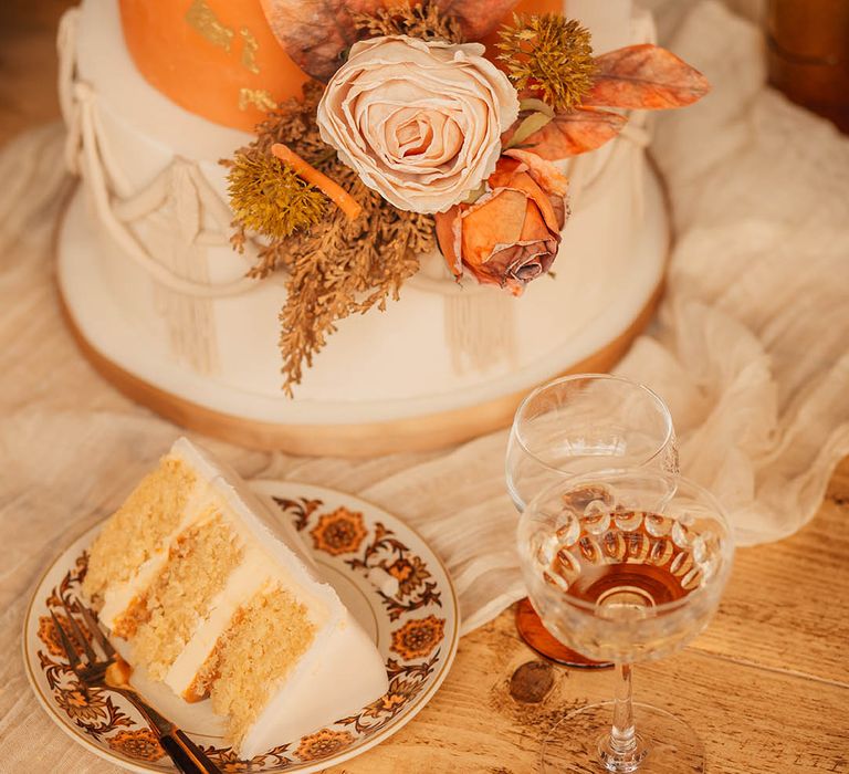 Plate with slice of wedding cake in front of three tier orange and white iced wedding cake 