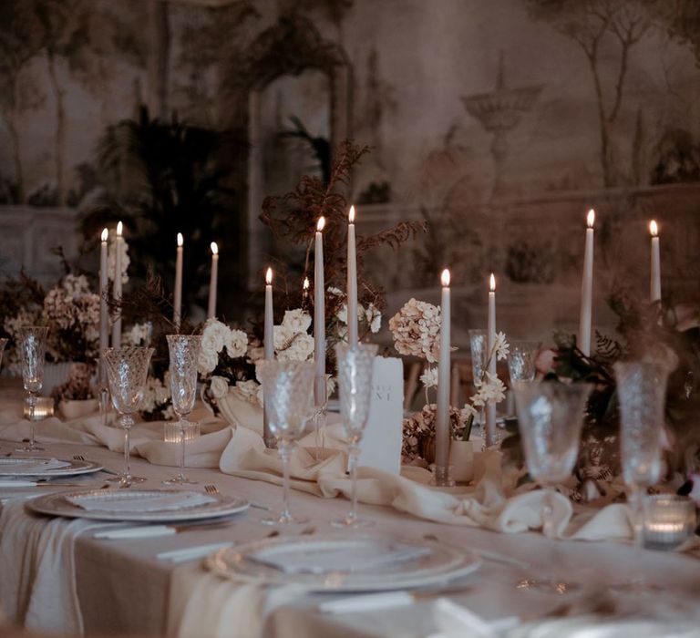 Romantic wedding table decor with warm candlelight and crystal wineglasses alongside flowers 