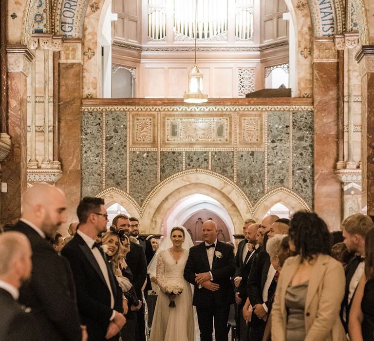 Father of the bride in black tie walks the bride down the aisle 