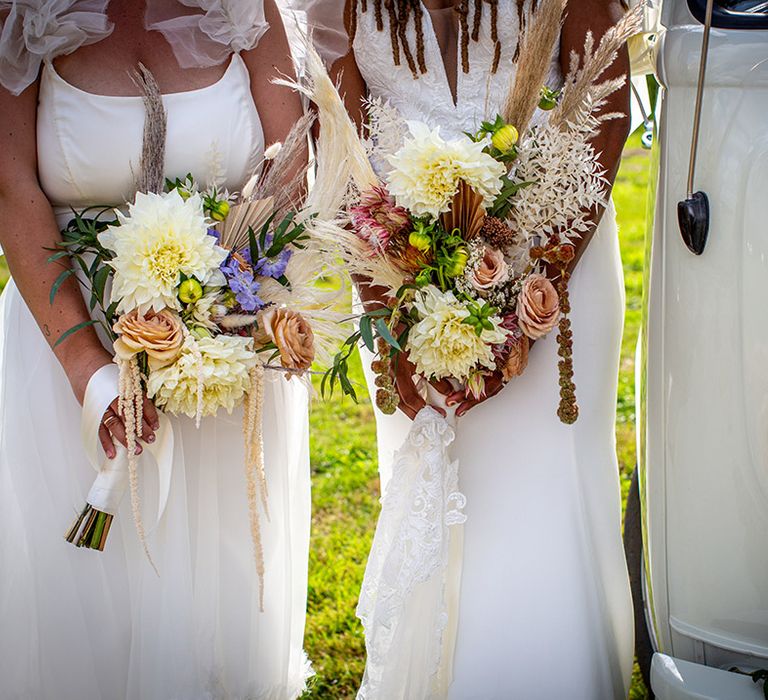 Two brides holding neutral wedding bouquets with pampas grass, dried palm leaves, dahlias and more 