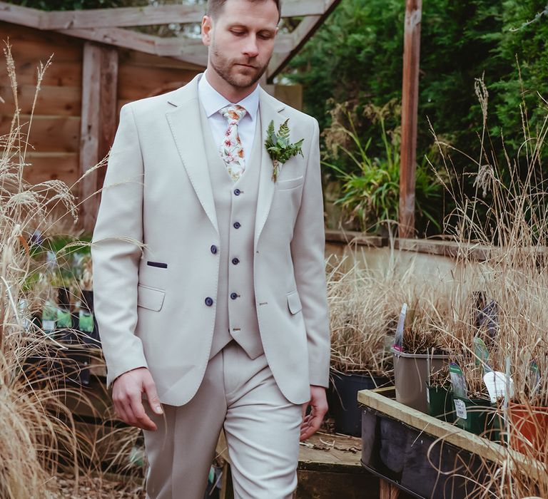 Groom in three piece light grey wedding suit with floral patterned tie with foliage buttonhole accessory 