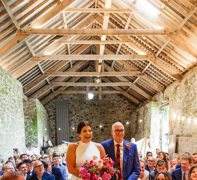 Father of the bride in blue wedding suit walking bride down the aisle at barn wedding 