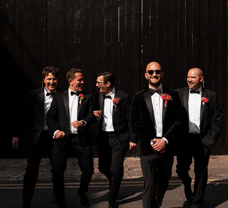 Groom and groomsmen in black tuxedos with pink flower buttonhole 